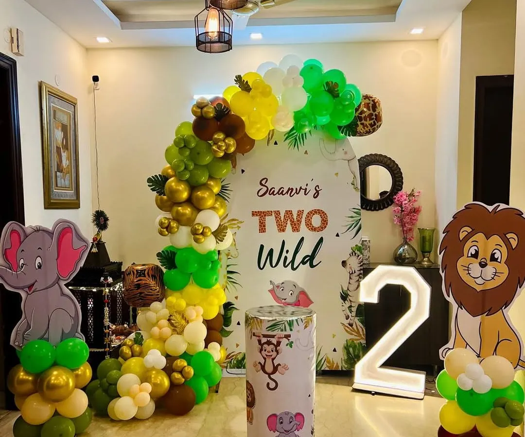 We transformed this living room into a "Two Wild" jungle safari for a second birthday party. This setup includes a personalized backdrop, a full balloon arch in jungle colors, cute animal cutouts of a lion and elephant, and a light-up number '2'.