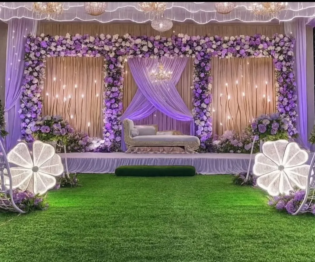 For a grand Sangeet or reception, I can design an elegant stage like this one. It uses a beautiful lavender and white floral theme, soft drapery, and unique lighted floral props to create a magical atmosphere for your celebration.