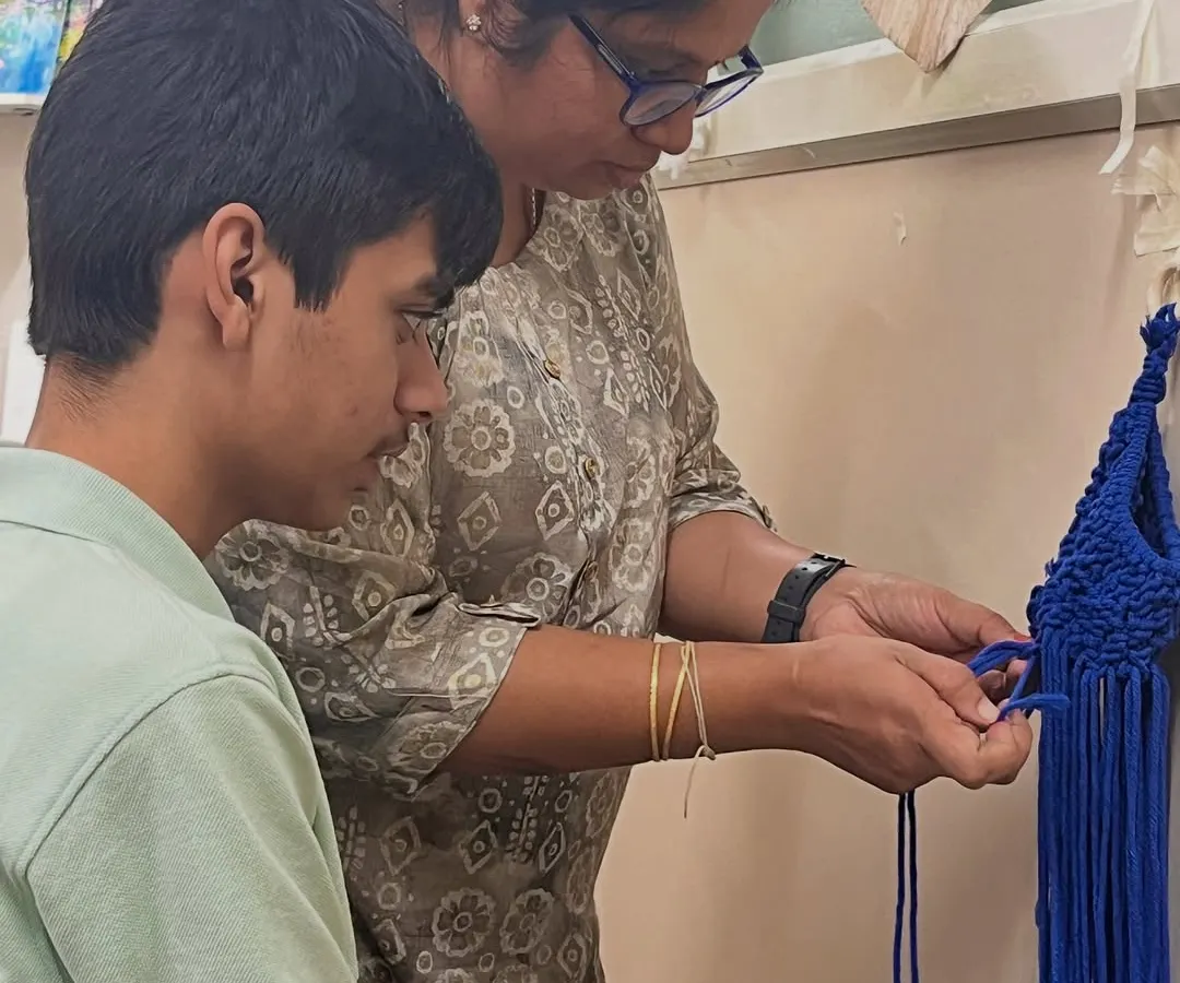 I believe in gentle, one-on-one guidance. Here, I'm helping a student with a macrame knot, ensuring he feels supported and confident as he learns this new skill. This adaptive instruction is at the heart of our special needs art program.
