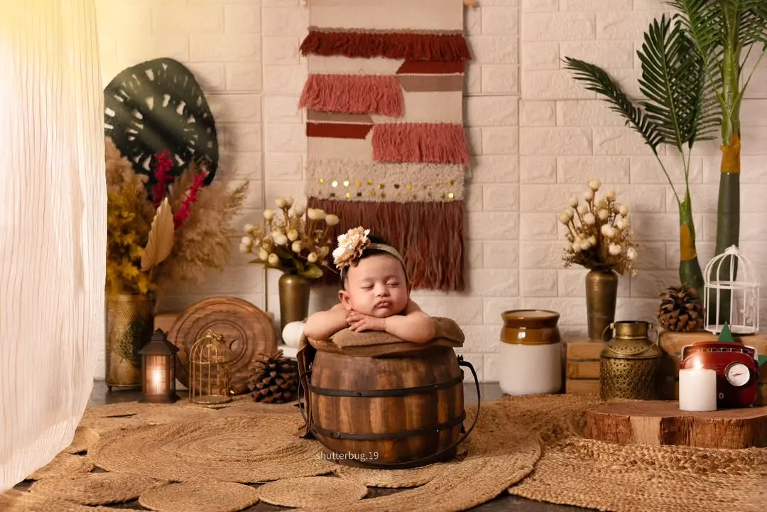 This little one looks so serene posing in a rustic wooden bucket as part of our popular boho-themed newborn shoot. We use natural textures like jute, wood, and macrame to create a warm, earthy, and timeless look.