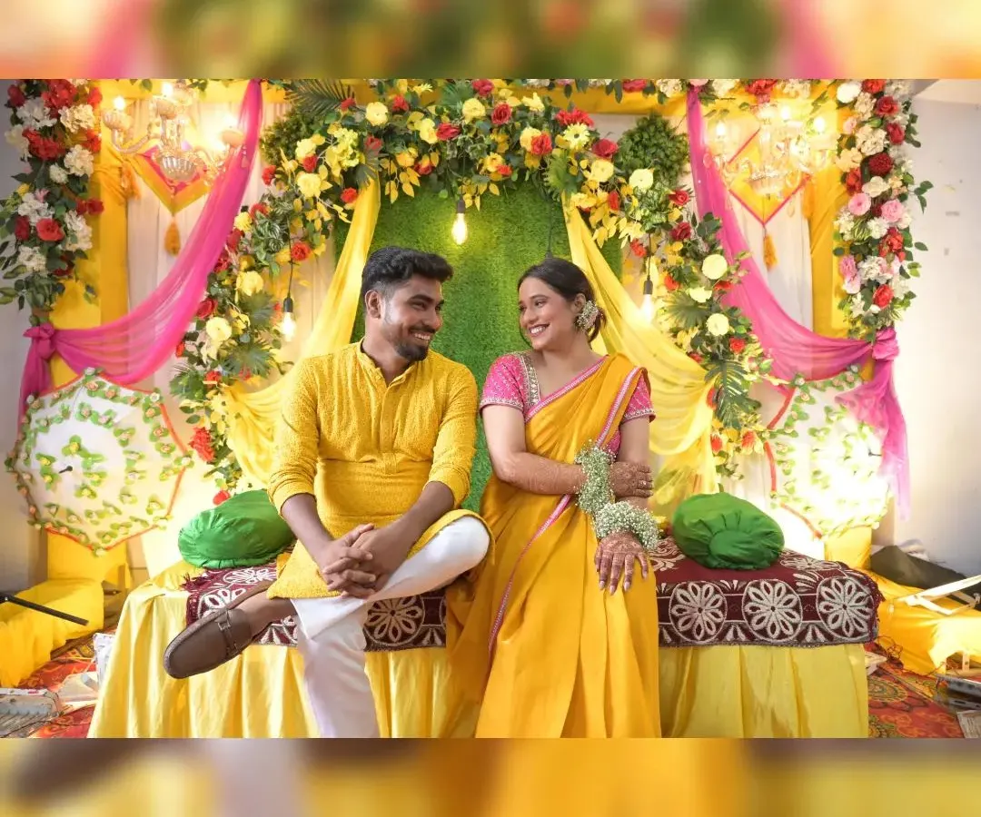 We create stunning backdrops for traditional Haldi ceremonies. This setup features a vibrant mix of yellow and pink drapes, a lush floral arch with marigolds and roses, and elegant hanging chandeliers to create a festive atmosphere.