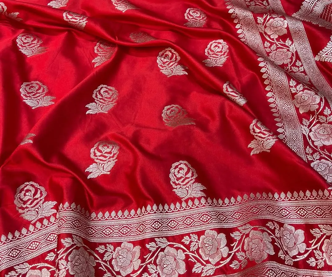 The vibrant red of this Banarasi Mashru silk saree is simply stunning. The silver rose motifs are woven directly into the fabric, creating a luxurious texture and timeless appeal for bridal or festive wear.