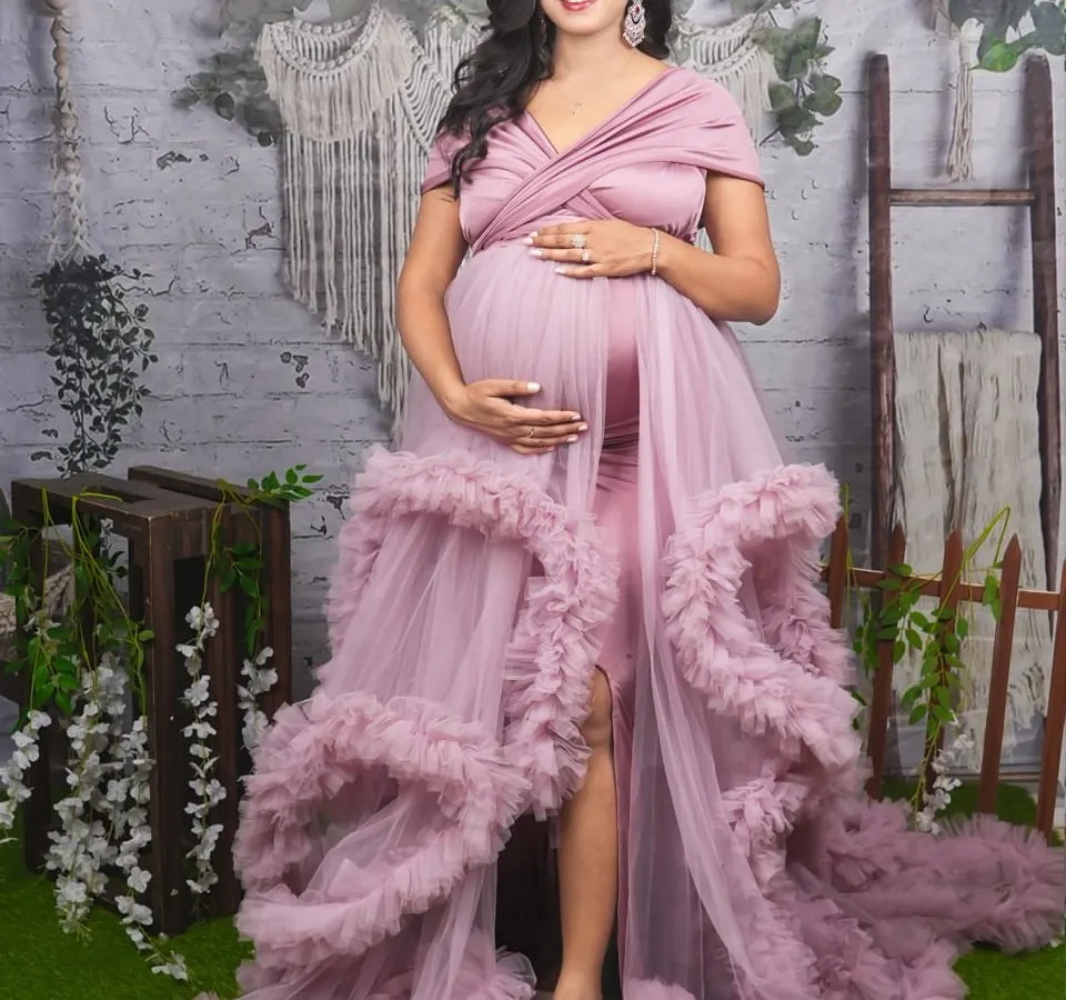 A full-length studio portrait showing off a beautiful dusty pink ruffled gown with a high slit. This style is perfect for highlighting your baby bump while adding a touch of glamour and sophistication to your maternity photos.