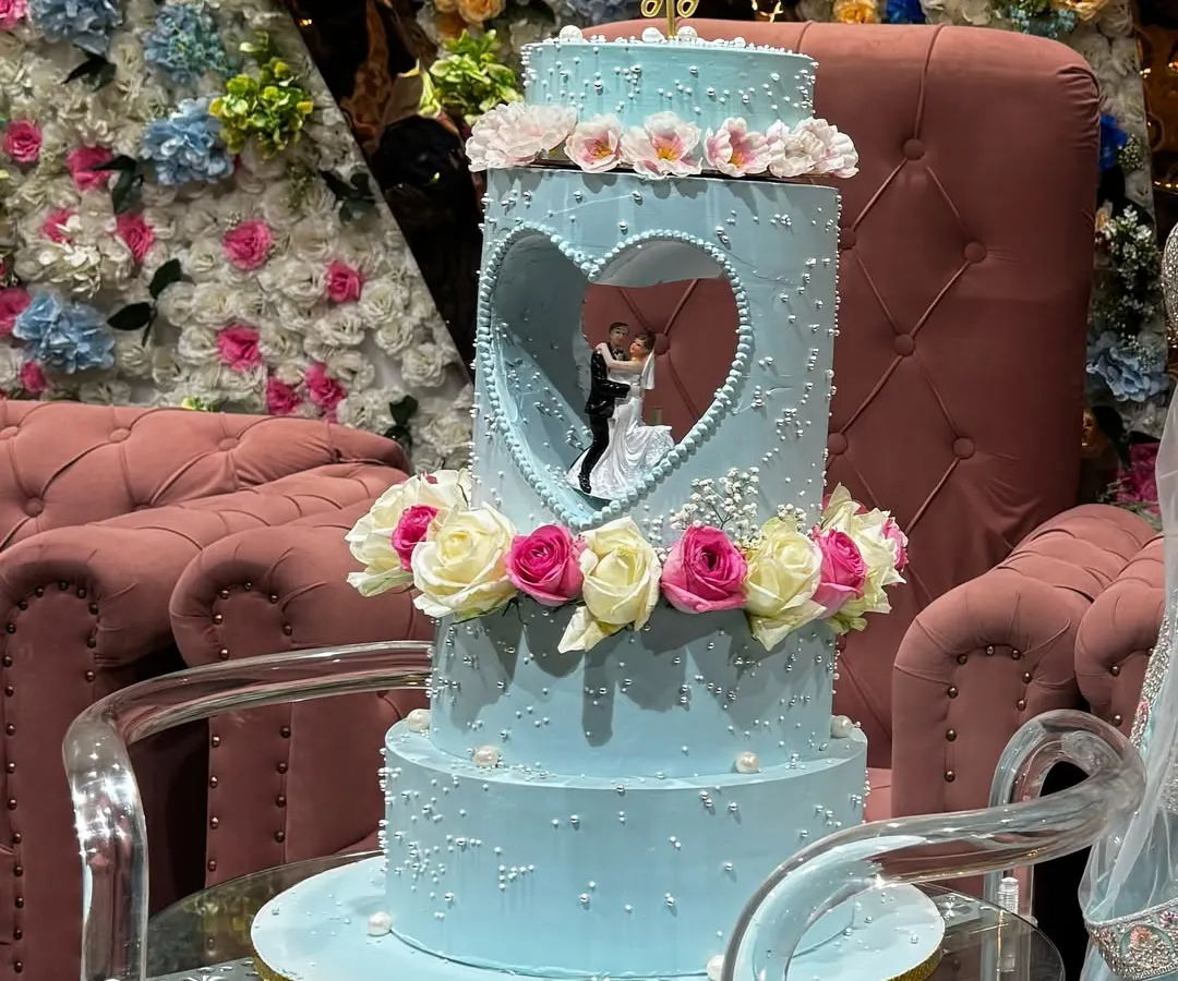 This breathtaking three-tier engagement cake features a unique heart-shaped cutout, revealing a delicate figurine of the couple. The soft blue frosting, pearl details, and fresh roses create a truly romantic and unforgettable centerpiece for a special engagement party.