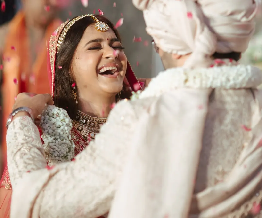 There's nothing like the pure joy of a bride on her wedding day. This candid shot captures that perfect moment of laughter, with her classic red lehenga and radiant makeup shining through.