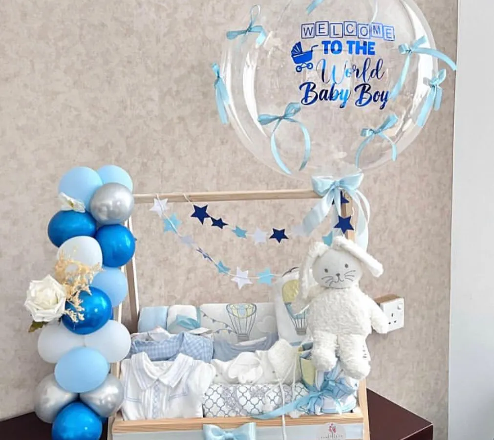 Welcoming a new baby boy is a huge deal, and this hamper is designed to match the occasion. We created a custom wooden clothing rack filled with baby essentials, complete with a personalized "Welcome to the World" balloon arrangement in shades of blue and silver.