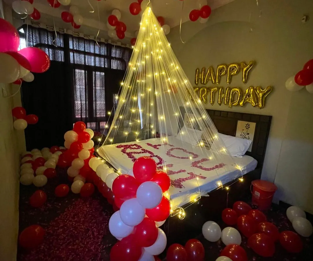 This is my classic romantic birthday decoration, perfect for surprising your partner. I use a canopy of fairy lights to create a dreamy focal point over the bed, complemented by hundreds of red and white balloons and rose petals on the bed and floor.