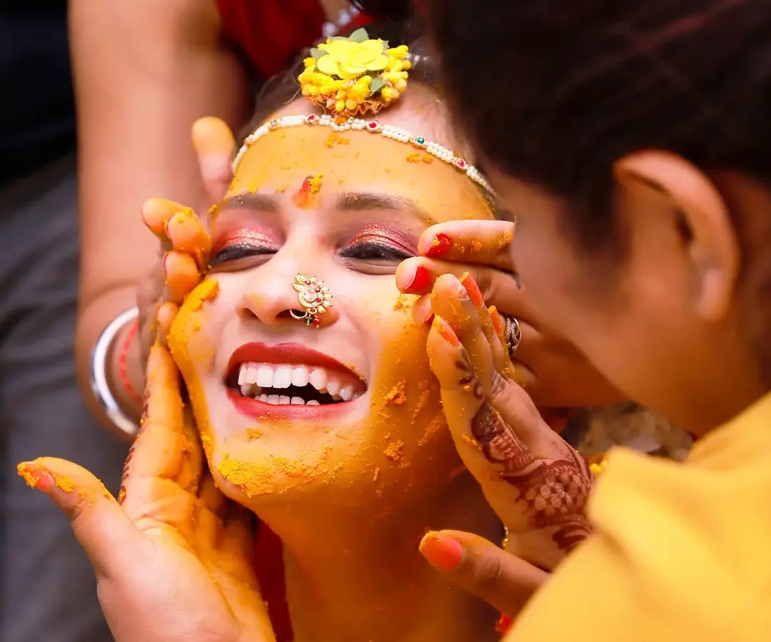 A candid shot capturing the pure joy of a bride during her Haldi ceremony, her face lit up with a wide smile as family applies turmeric paste. These unscripted moments of happiness are what make wedding photography so special.