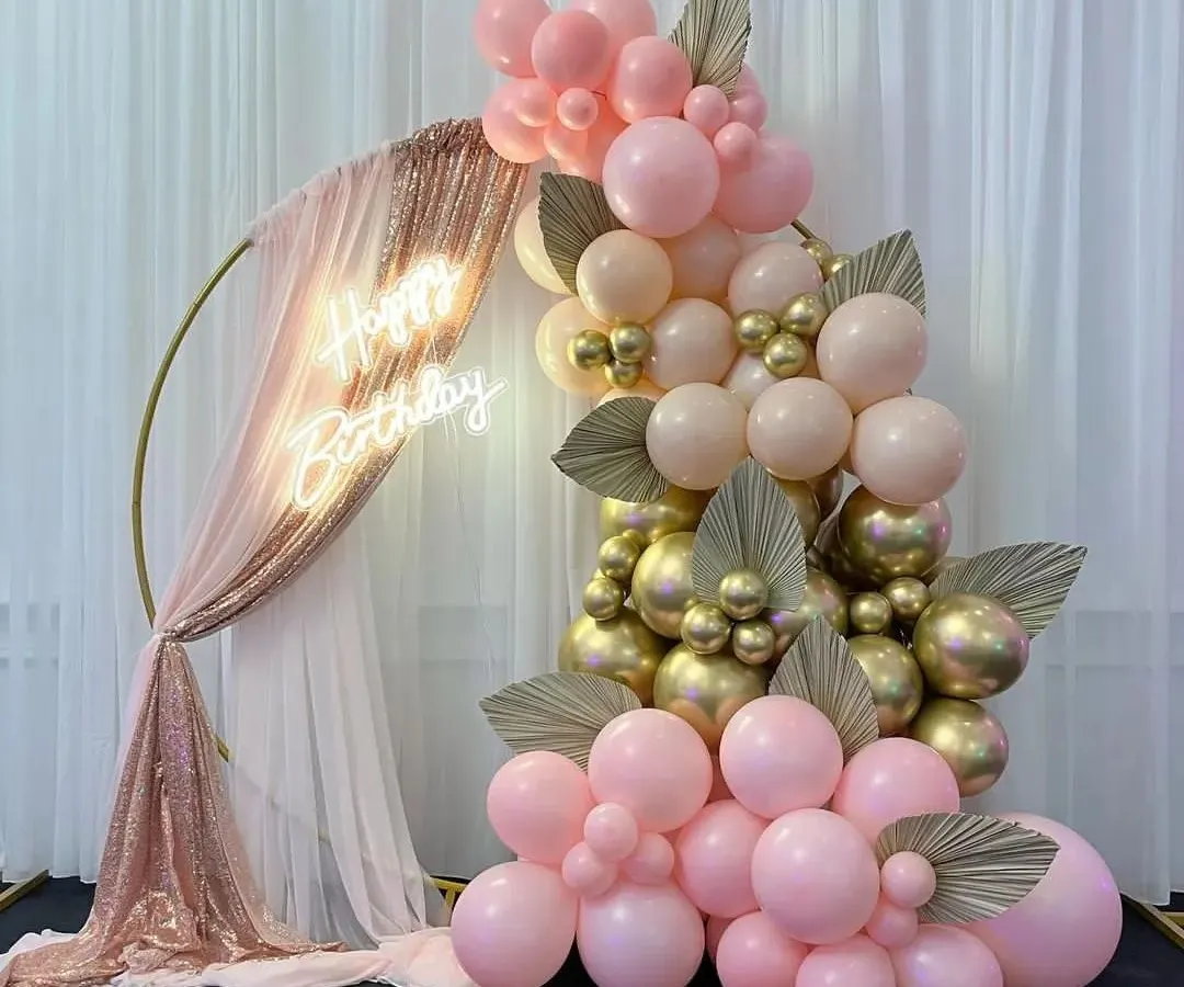 I love creating elegant and chic setups like this one. This beautiful photo corner features a gold ring draped with sequined and sheer fabric, a custom 'Happy Birthday' neon sign, and a stunning balloon cascade in pink, peach, and chrome gold.