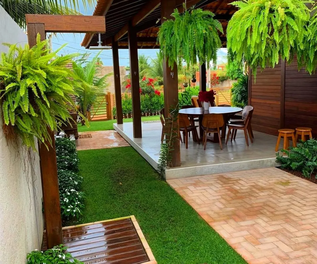 We design outdoor living areas that feel like a natural extension of your home. Here, a covered patio is enhanced by lush hanging ferns and a perfectly manicured lawn, creating a private escape for relaxation and entertainment.