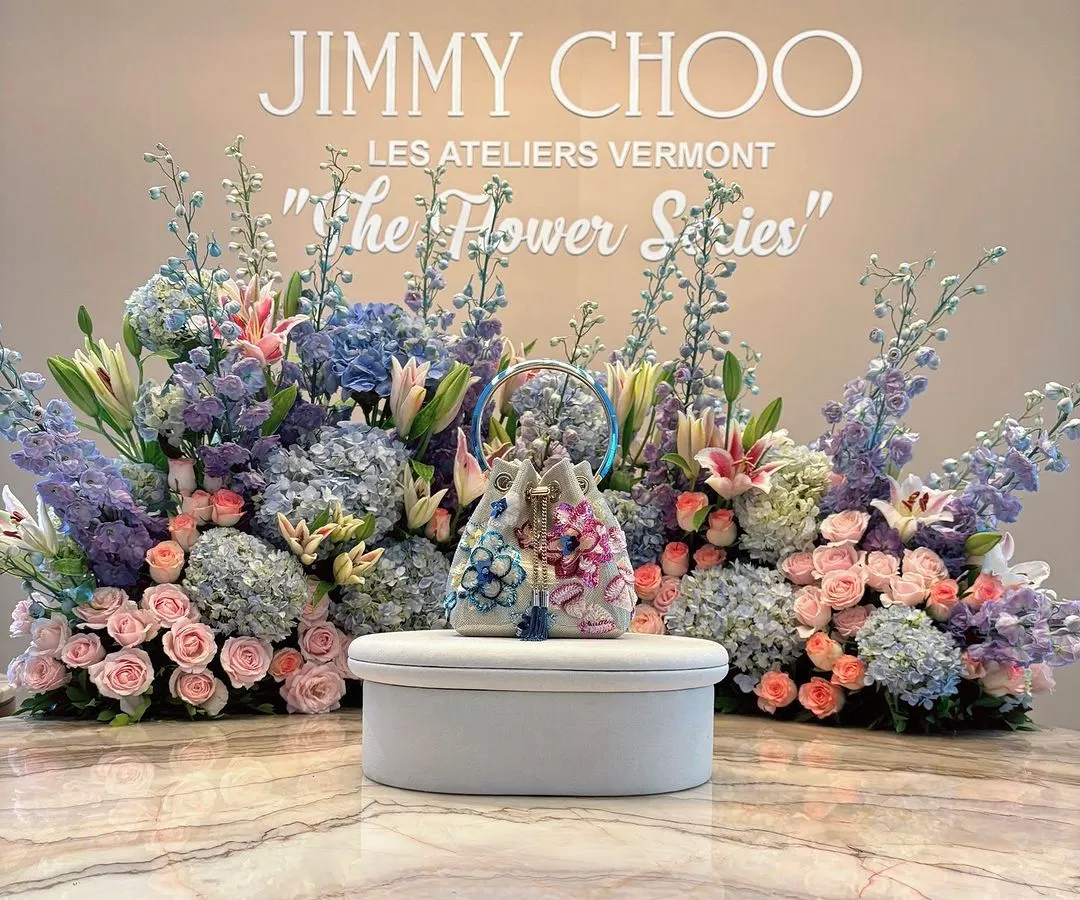 A product display designed for the launch of Jimmy Choo's 'The Flower Series'. The new handbag is presented on a pedestal, framed by an exquisite arrangement of pastel hydrangeas, roses, and lilies, perfectly reflecting the collection's floral elegance.