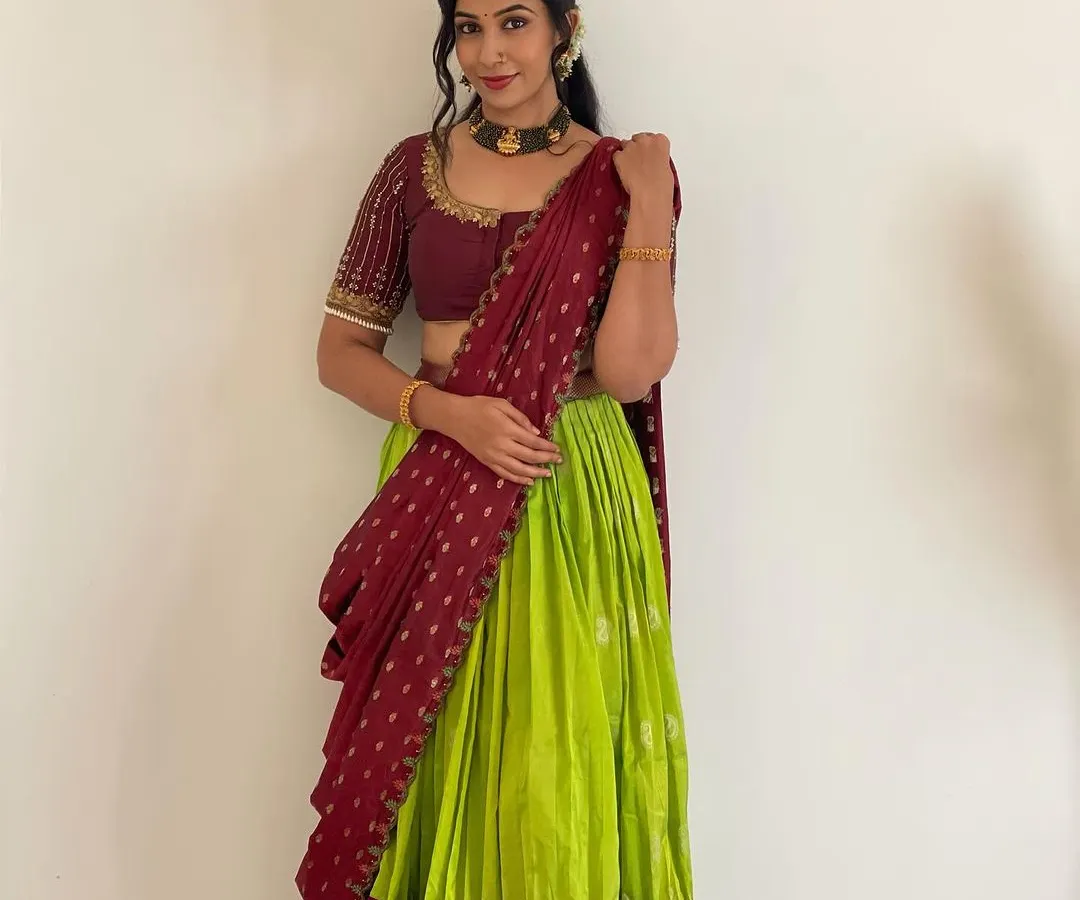 A classic langa voni or half saree in a vibrant lime green and maroon combination. This traditional outfit is perfect for festivals and family functions, designed to be both beautiful and comfortable. The blouse features delicate handwork on the sleeves.