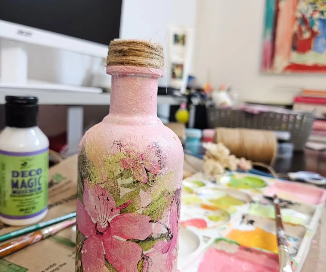 Here is a look at one of my one-of-a-kind decoupage pieces. I love transforming simple glass bottles into unique home decor items. This one features a soft pink texture and delicate floral motifs, perfect for a boho chic space.