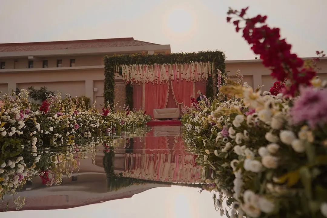 We love creating dreamlike settings, like this serene daytime mandap. The floral aisle, reflected perfectly in the water, leads to a stage adorned with fresh blooms and delicate pink drapes, making for a truly picturesque wedding ceremony.