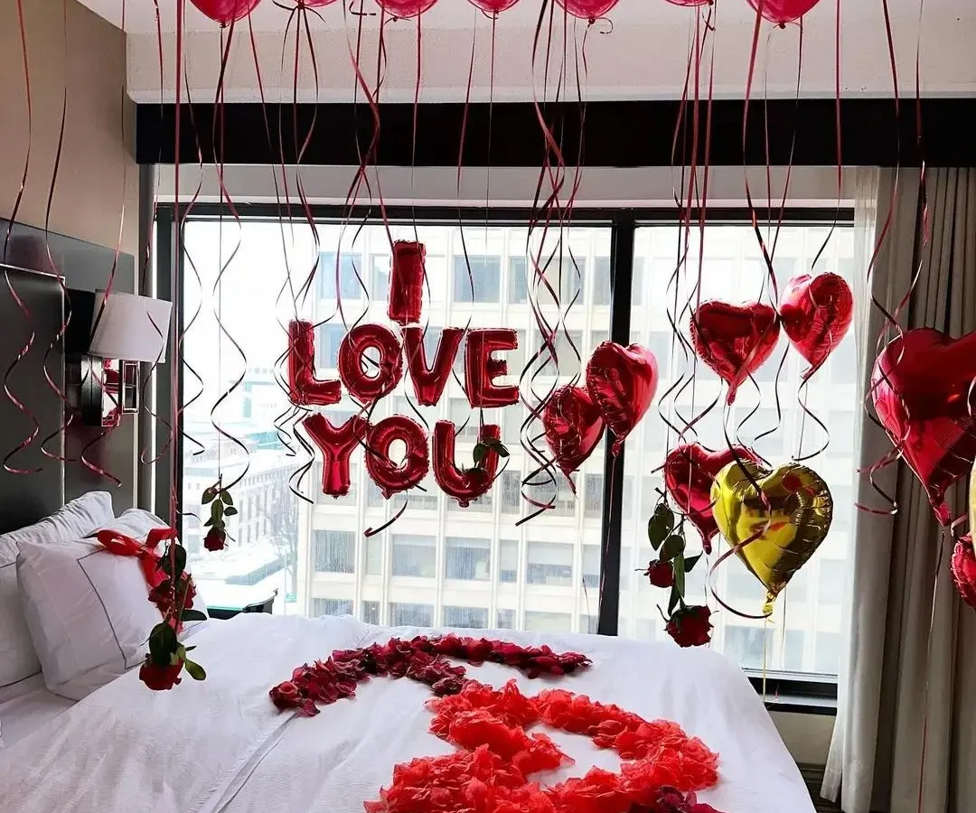 This is our classic romantic room decoration, perfect for proposals and anniversaries. The setup includes a ceiling filled with red balloons, 'I LOVE YOU' foil letters above the bed, and heart-shaped balloons framing the window view.