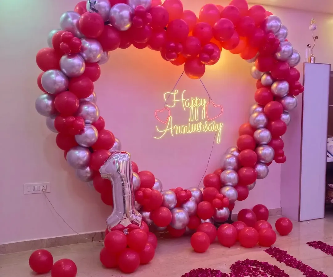 Apni pehli anniversary ko khaas banane ke liye humne yeh red aur silver chrome balloons ka heart shape frame taiyar kiya hai. Beech mein 'Happy Anniversary' ka neon sign iski sundarta aur badha raha hai.