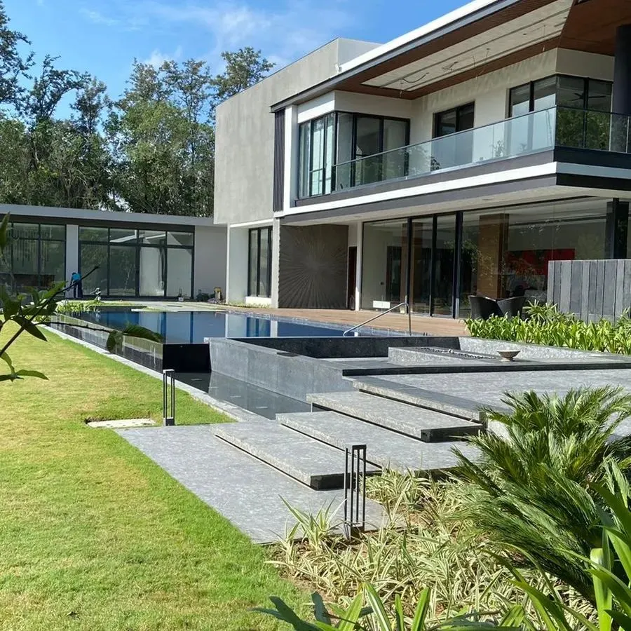 The expansive view of a modern Delhi farmhouse, where a pristine swimming pool and manicured lawn meet contemporary architecture. This project showcases our ability to create seamless transitions between indoor comfort and outdoor splendor, featuring clean lines and lush greenery.