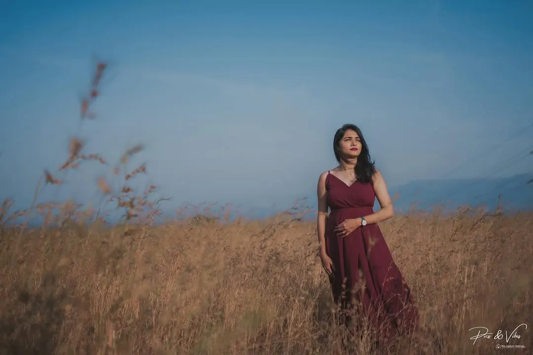 Bathed in the magic of golden hour, this outdoor maternity photo captures a moment of serene reflection. The expecting mother stands in a field of tall grass, her gown flowing, creating a beautiful and cinematic pregnancy portrait against the vast sky.