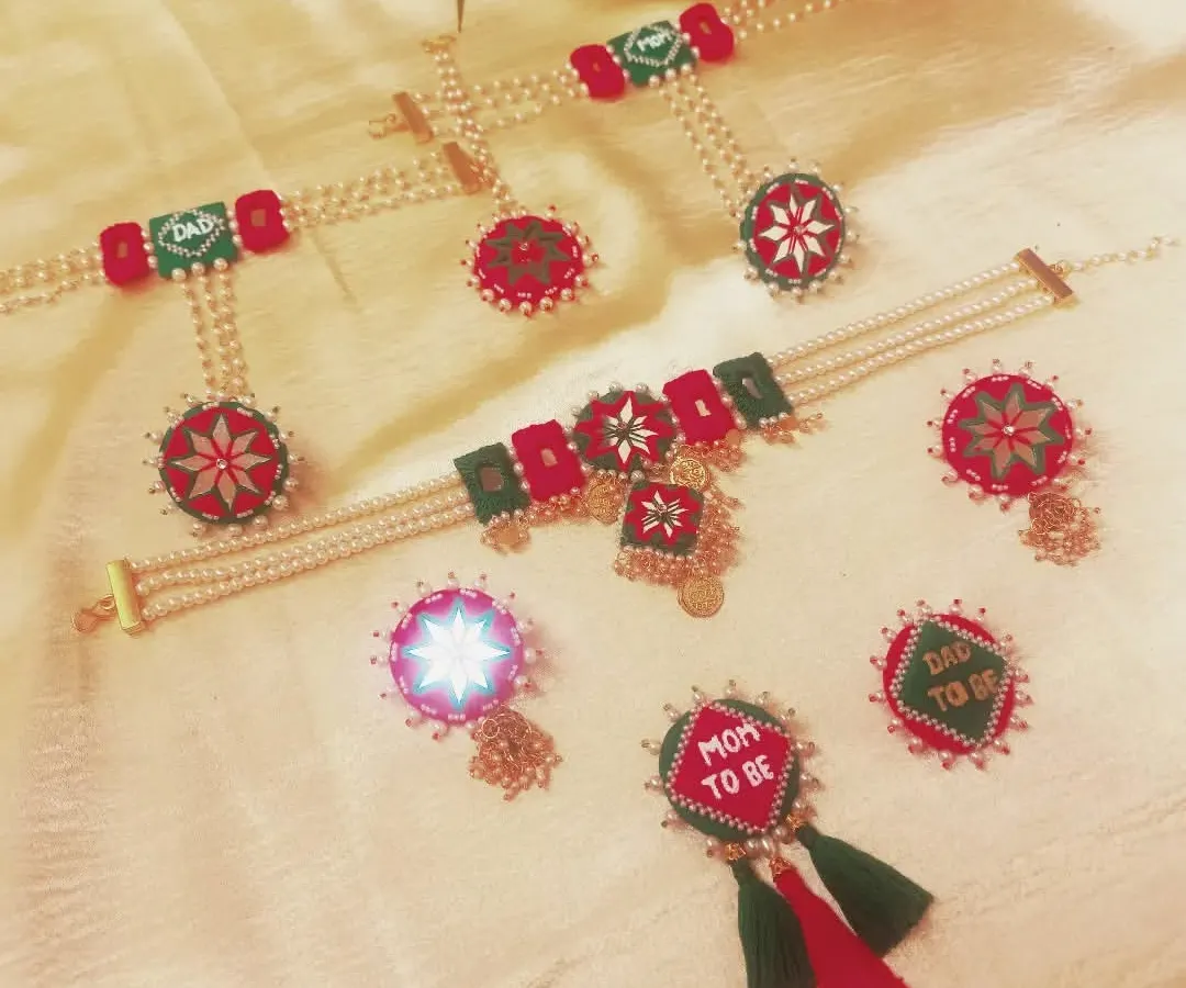 This is a complete baby shower jewelry set I created for a client. It includes a 'Mom to be' and 'Dad to be' brooch, necklace, earrings, and mathapatti, all handcrafted with fabric and pearls in a festive red and green theme.