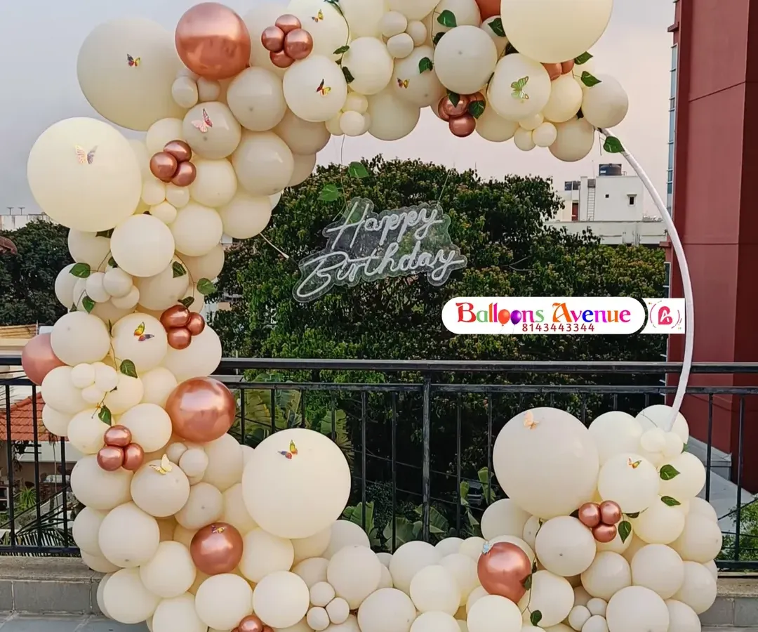 Our decorations are perfect for any location, including this beautiful outdoor terrace setup in Bangalore. This features an elegant circular frame adorned with a dense arch of pastel and rose gold chrome balloons, butterfly accents, and a central 'Happy Birthday' neon sign, creating a perfect photo opportunity.