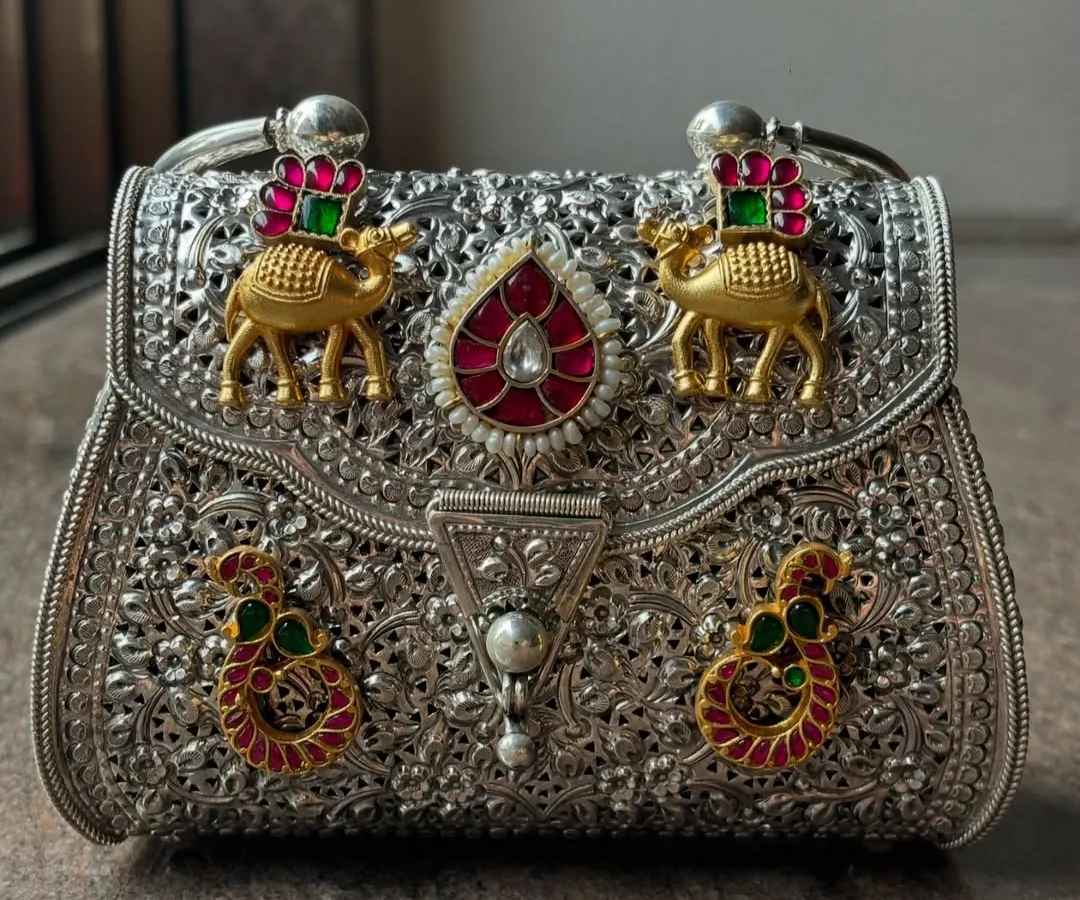 This is where tradition meets trend. A close-up of our bespoke fusion clutch, featuring intricate silver filigree work with gold plating and colourful stone embellishments like camels and paisleys. It’s a statement piece that tells a story.
