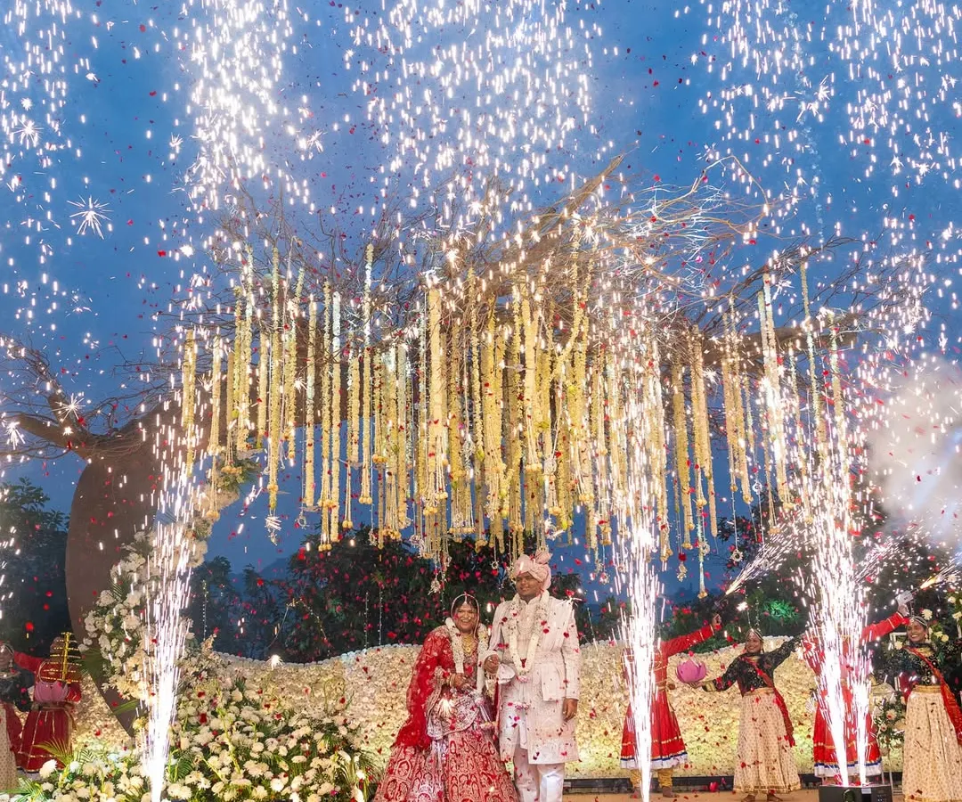 Under a sky lit by fireworks, this couple exchanged garlands beneath a custom-designed 'tree of life' mandap. This spectacular Varmala moment at a Lonavala resort combined rustic charm with explosive celebration, a perfect reflection of their vibrant love story.