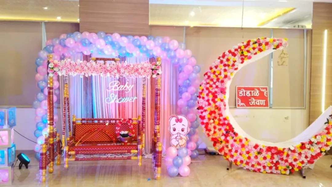 For this 'Dohale Jevan' baby shower, I combined modern and traditional elements. The setup features a large pastel balloon arch over a decorated swing (jhula) and a floral crescent moon photo point for guests.