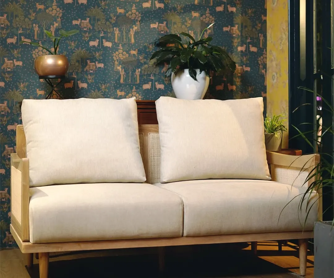 Our signature two-seater sofa combines a solid Teak wood frame with delicate, handwoven cane panels. This piece exemplifies our commitment to blending traditional craftsmanship with clean, modern lines for a timeless aesthetic.