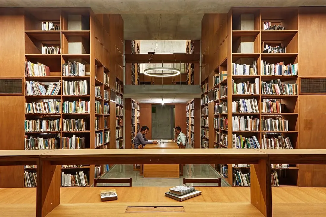 We design libraries as sanctuaries for knowledge and quiet contemplation. At the Lilavati Lalbhai Library at CEPT University, floor-to-ceiling wooden bookshelves create a warm, immersive environment, with carefully planned sightlines that draw the eye through the multi-level, subterranean space.