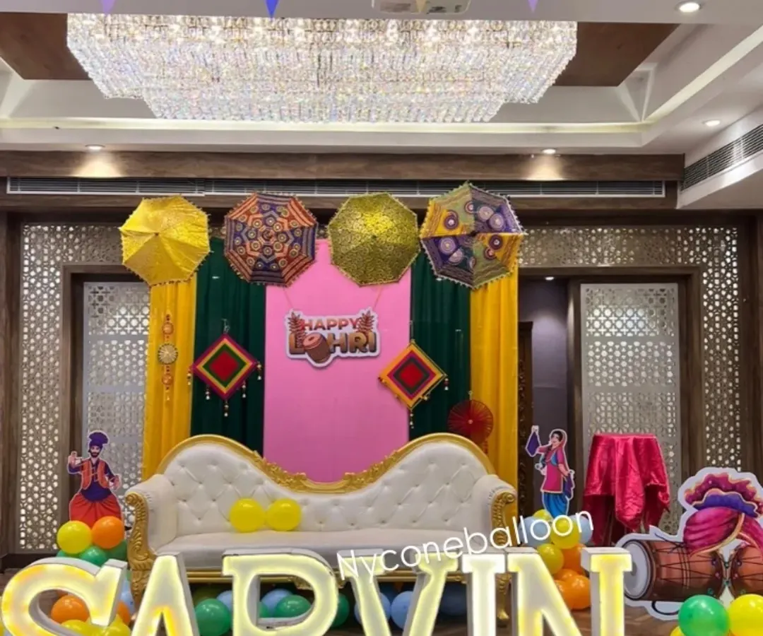 For baby Sarvin's first Lohri, I created this personalized stage featuring large, illuminated letters of his name. The setup includes a comfortable sofa for the family, colorful drapes, and festive Punjabi elements like decorative umbrellas.