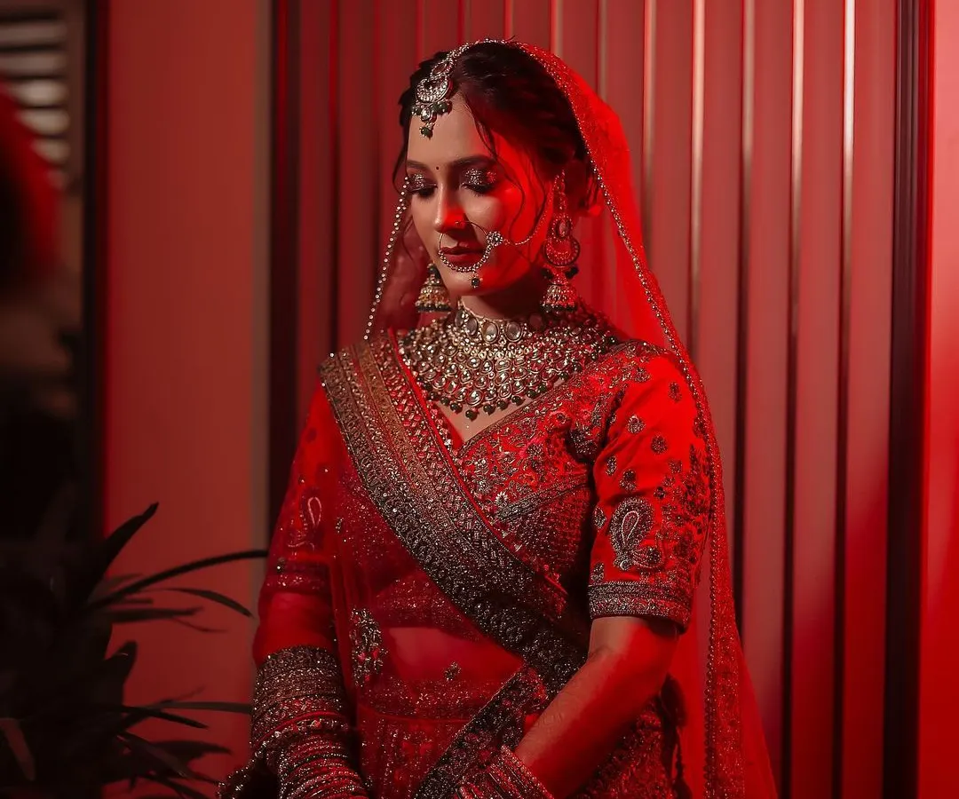 A stunning bridal portrait using dramatic red lighting to create a bold, cinematic feel. This shot highlights the bride's serene expression and the intricate details of her red lehenga and jewelry.