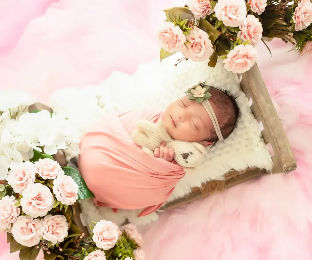 A peaceful newborn girl, swaddled in soft pink and surrounded by a bed of delicate roses. Our newborn photography sessions prioritize your baby's comfort while creating beautifully styled portraits.