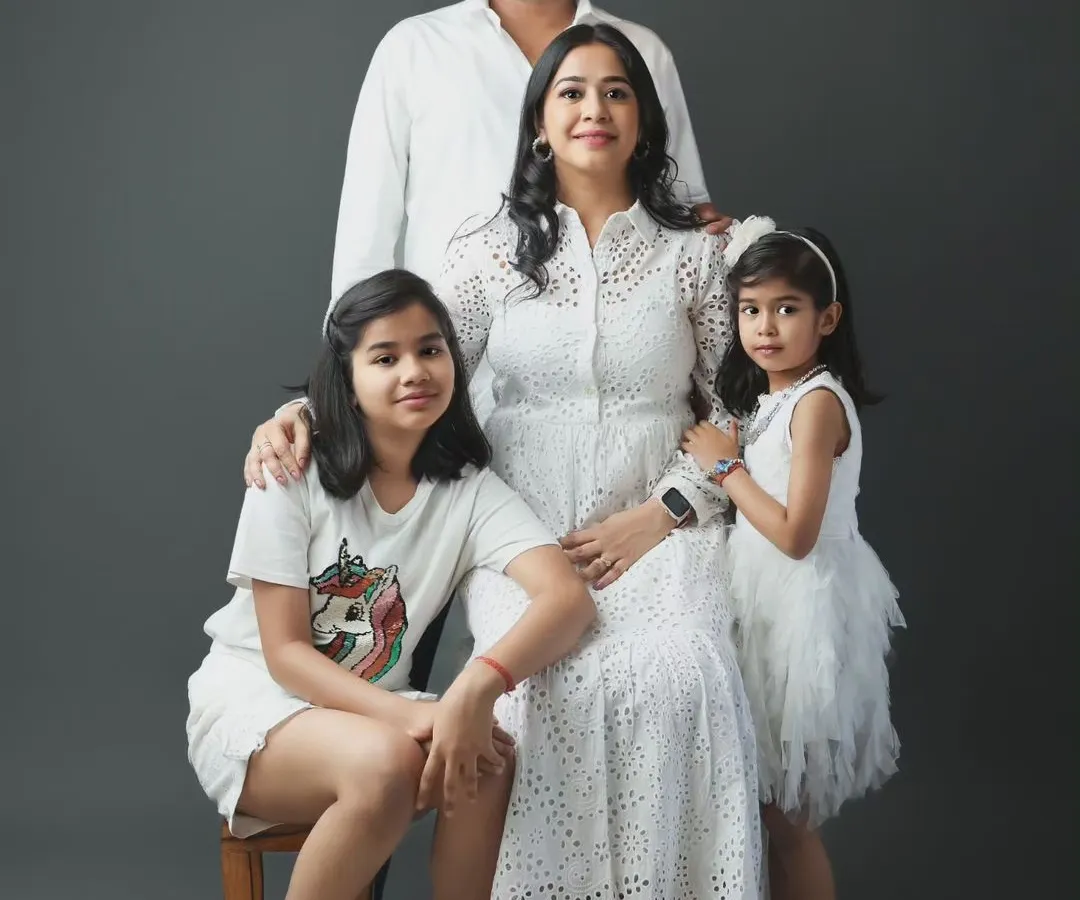 This is a classic family portrait from our Noida studio. We arranged this family of four, with parents and two daughters, for a timeless look against a simple grey backdrop, highlighting their connection and coordinated white outfits.