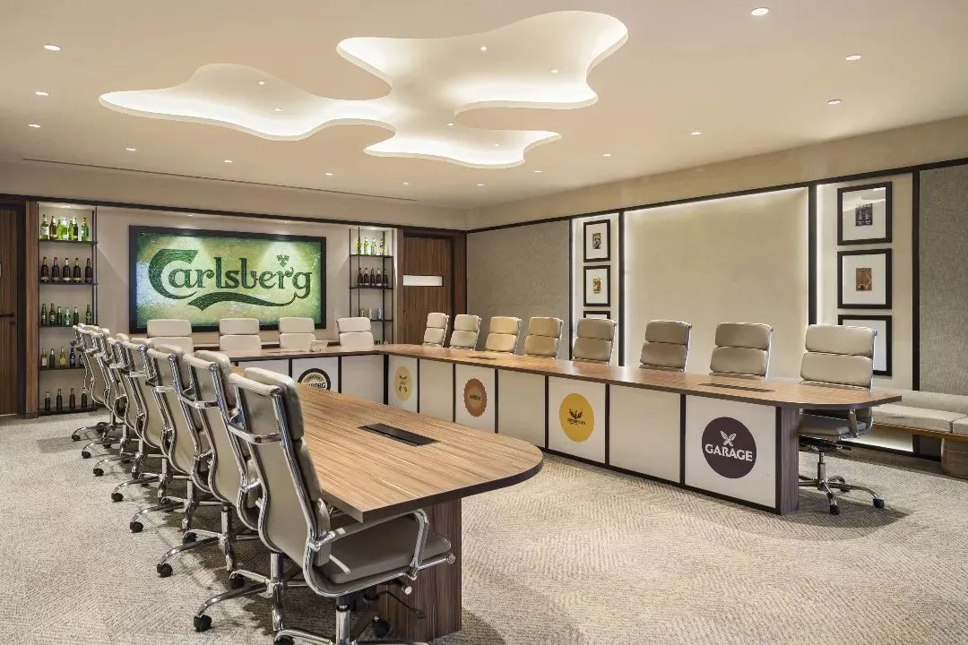 The boardroom at the Carlsberg Head Office in Gurugram, a space designed to reflect brand legacy and foster collaboration. The design integrates the company's iconic identity through custom elements, including a unique ceiling feature and brand logos on the conference table, creating a powerful, immersive corporate environment.