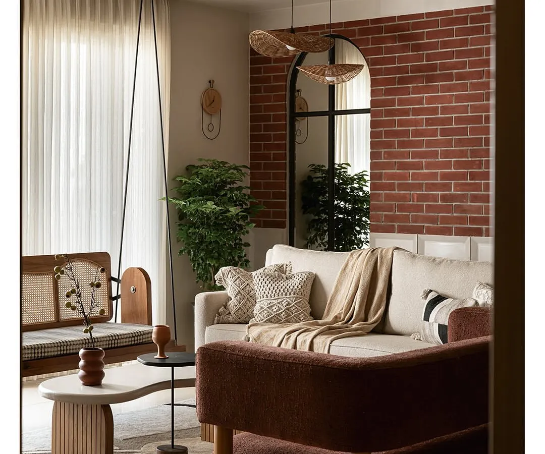 As you enter this living area, an exposed brick wall creates a warm, earthy backdrop. I placed a large arched mirror to reflect natural light, making the space feel larger and connected to the outdoors. The custom reversible cane swing, organic-shaped tables, and rich textures come together to create a grounded yet elegant feel.