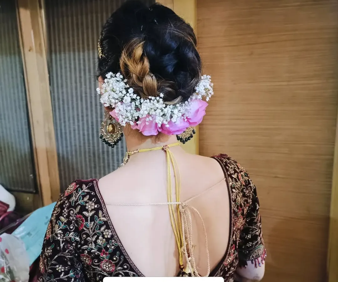 This is a classic bridal bun, intricately woven and adorned with a combination of fresh pink roses and delicate baby's breath. It's a secure and elegant choice that keeps the focus on the bride's profile and jewelry.