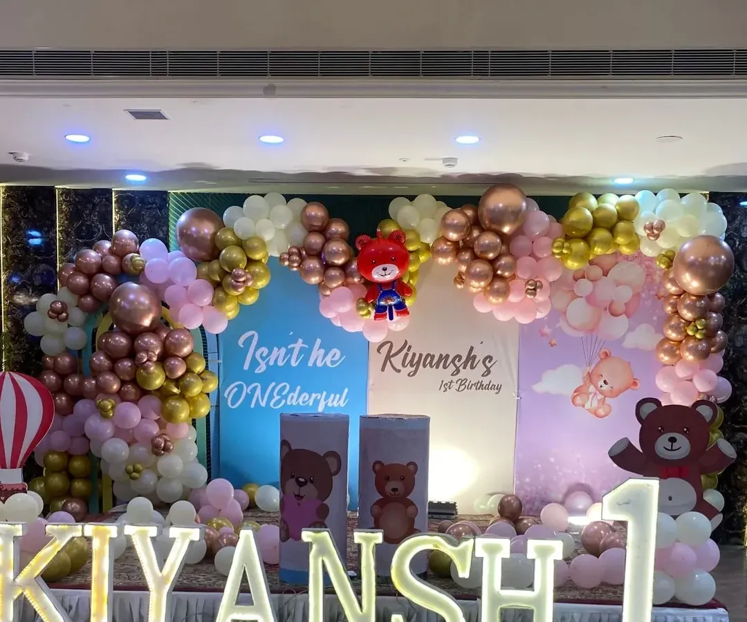 For a child's first birthday, I can create a magical world. This "ONEderful" teddy bear theme includes a full stage setup with custom backdrops, a multi-colored balloon arch with rose gold and chrome accents, and large marquee letters spelling out the birthday boy's name.