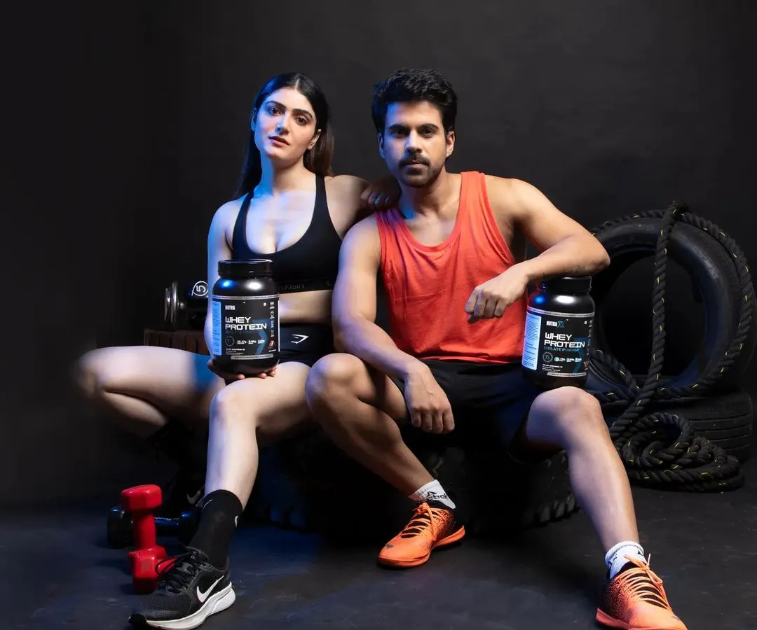 A key shot for e-commerce, featuring both male and female models presenting the whey protein supplements directly to the camera. This composition is effective for building trust and is ideal for landing pages or Amazon A+ content, clearly displaying the product in a relatable fitness context.
