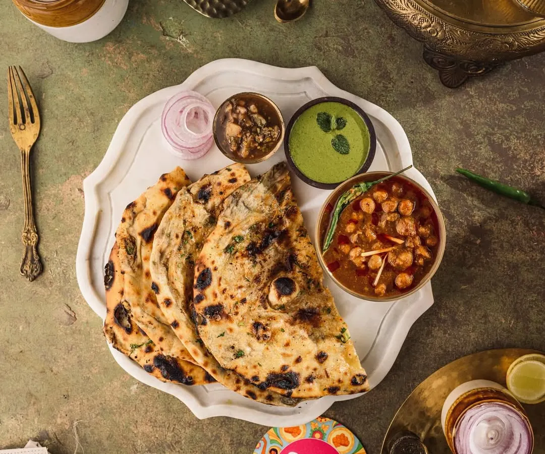 A top-down shot capturing a classic North Indian meal. I used a dark, moody style to highlight the rich textures of the garlic naan and the deep colors of the chole, creating a rustic and soulful image for Chew Chapad's menu.
