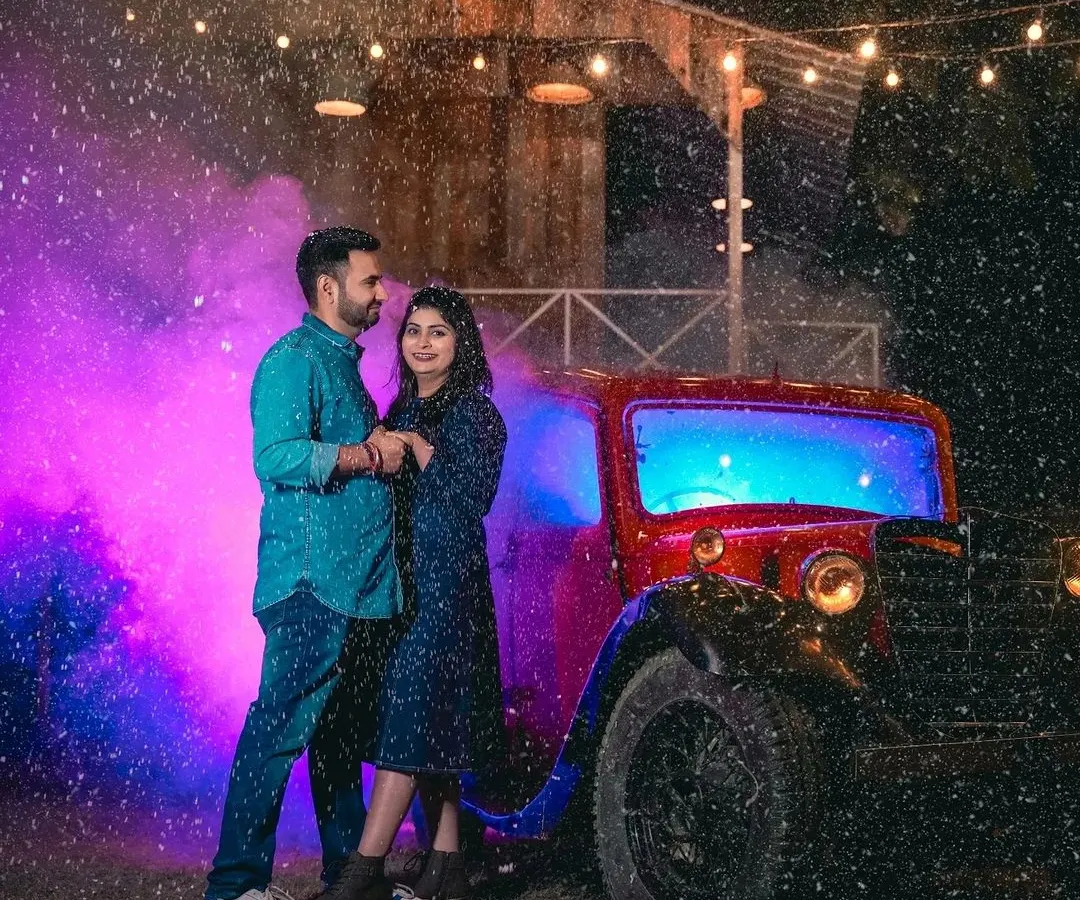 I use cinematic effects like artificial rain and colored smoke to add drama and emotion to your pre-wedding photos. Here, a couple shares a romantic moment by our vintage red car, creating a scene straight out of a movie.