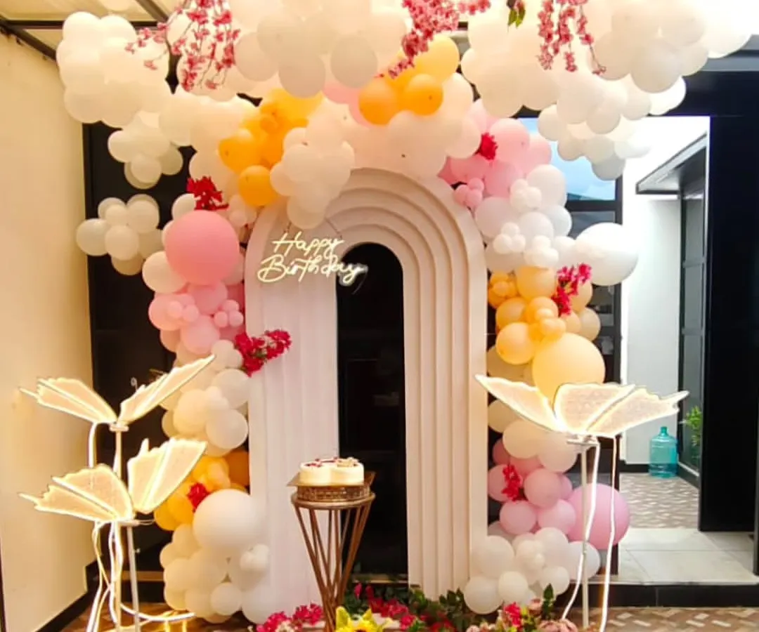 A dreamy birthday setup with balloon clouds, hanging floral arrangements, and illuminated leaf props. This unique design uses a modern arched backdrop and a neon 'Happy Birthday' sign to create a whimsical, picture-perfect celebration space.