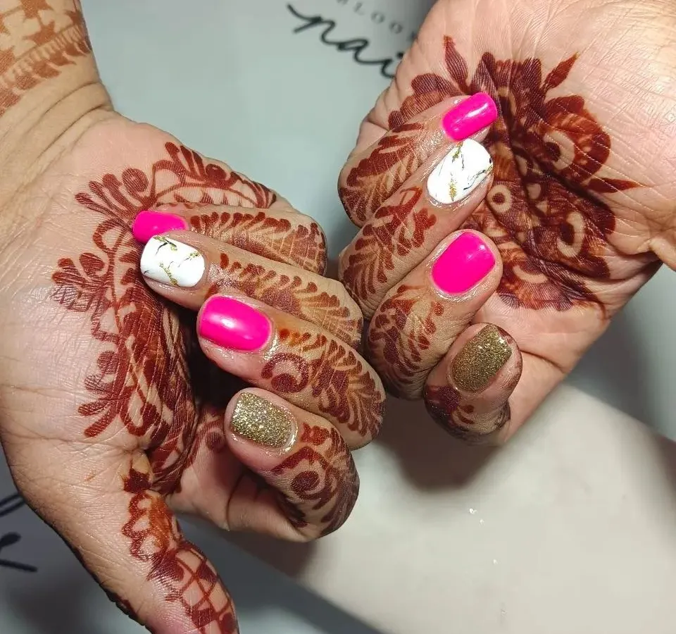 I am obsessed with creating the perfect bridal nails. This set features vibrant pink, gold glitter, and a white marble accent nail, all designed to complement the beautiful wedding mehendi.