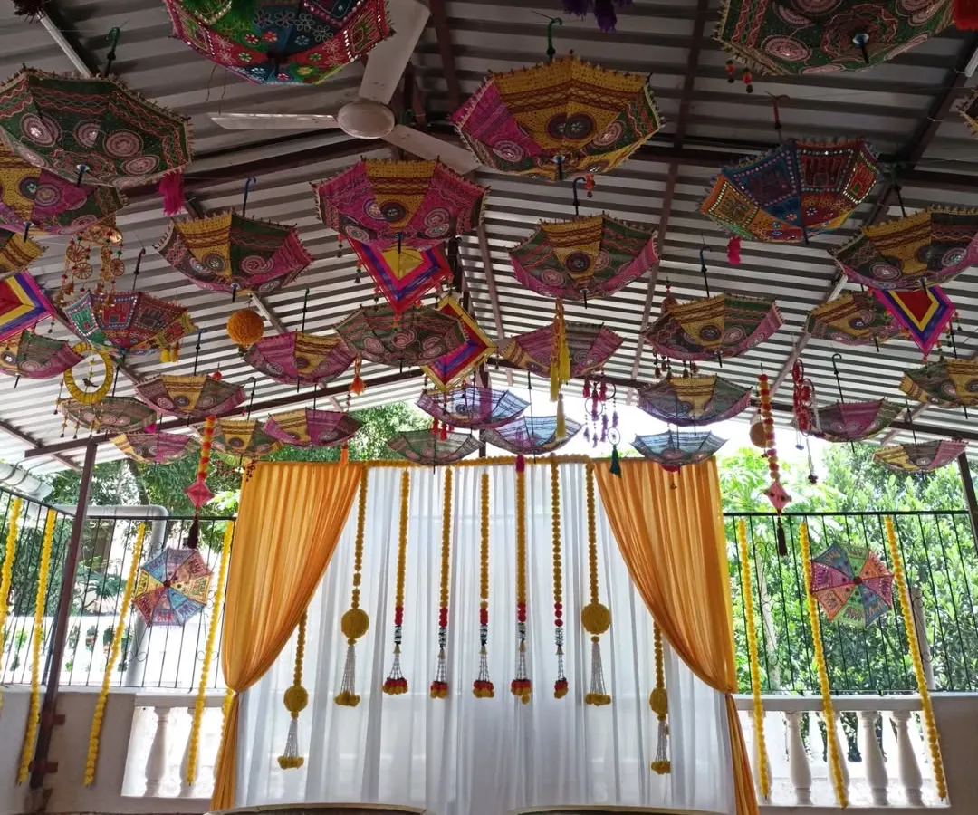 For a vibrant Haldi function, we created this beautiful outdoor setup. The ceiling is decorated with colorful Rajasthani umbrellas, while the backdrop features yellow and white drapes with traditional marigold flower strings.