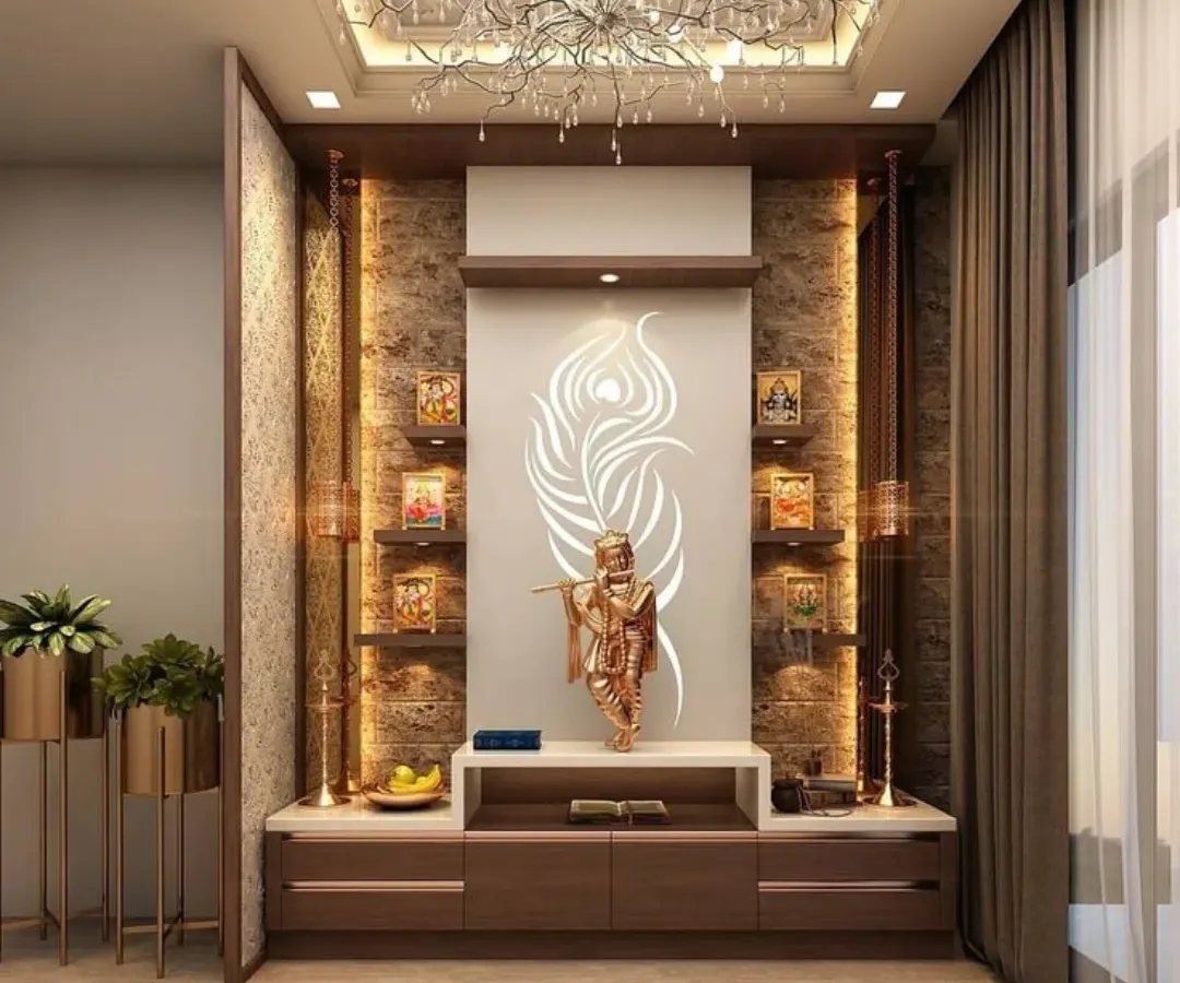 This mandir design blends warm wood tones with a textured stone backdrop for a contemporary yet earthy feel. A backlit panel featuring a peacock feather motif illuminates the Krishna idol, while tiered shelving and accent lighting provide space for smaller frames and decorative items.