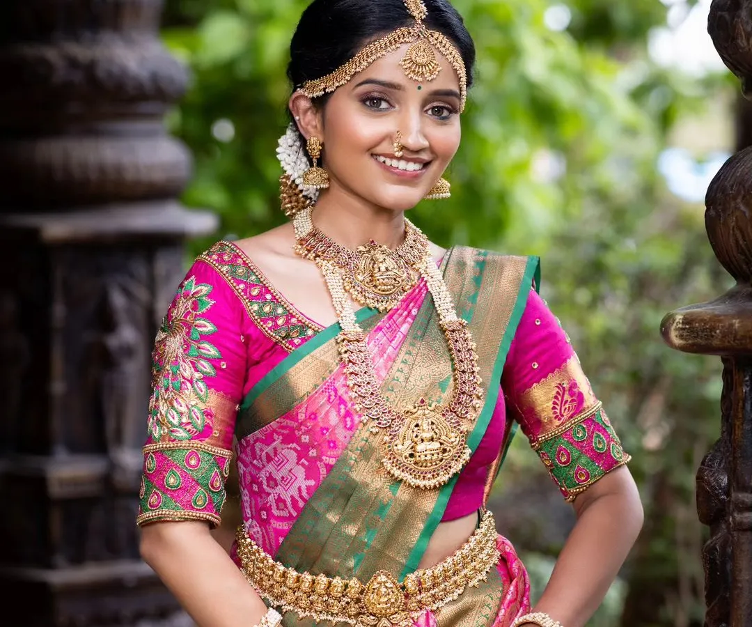 A classic South Indian bride in a stunning pink and green Kanjivaram silk saree. This timeless combination is perfect for Muhurtham ceremonies, offering traditional elegance and grace. The pure silk drapes beautifully for photos and makes you feel rooted in tradition.