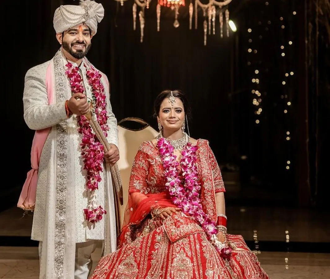 A classic wedding portrait that feels grand and timeless. I framed this shot to include the stunning chandelier, adding to the elegance of the moment. The couple is posed formally, showcasing the bride's magnificent red lehenga and the groom's coordinated white sherwani, capturing the complete look of their special day.