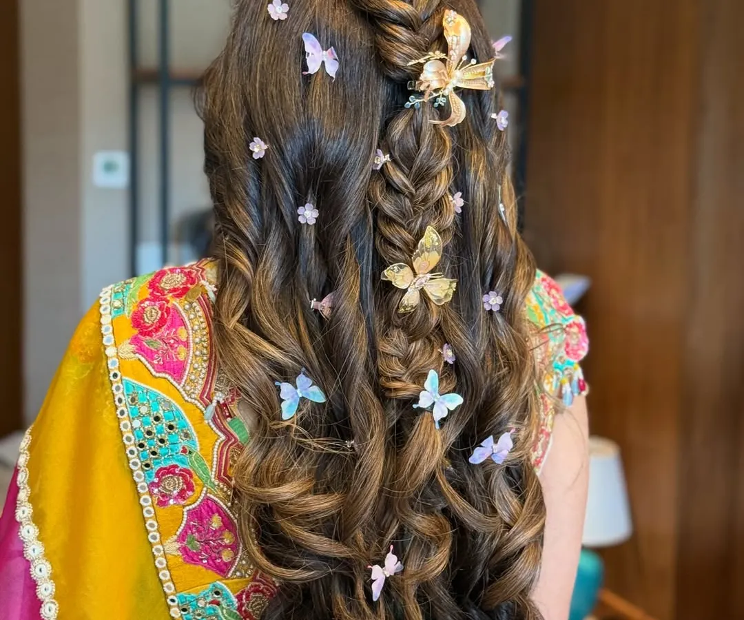 For a playful and whimsical Mehandi look, I created this half-up, half-down style featuring a fishtail braid and voluminous curls. The look is brought to life with an array of delicate butterfly clips in gold and pastel shades, adding a touch of magic.