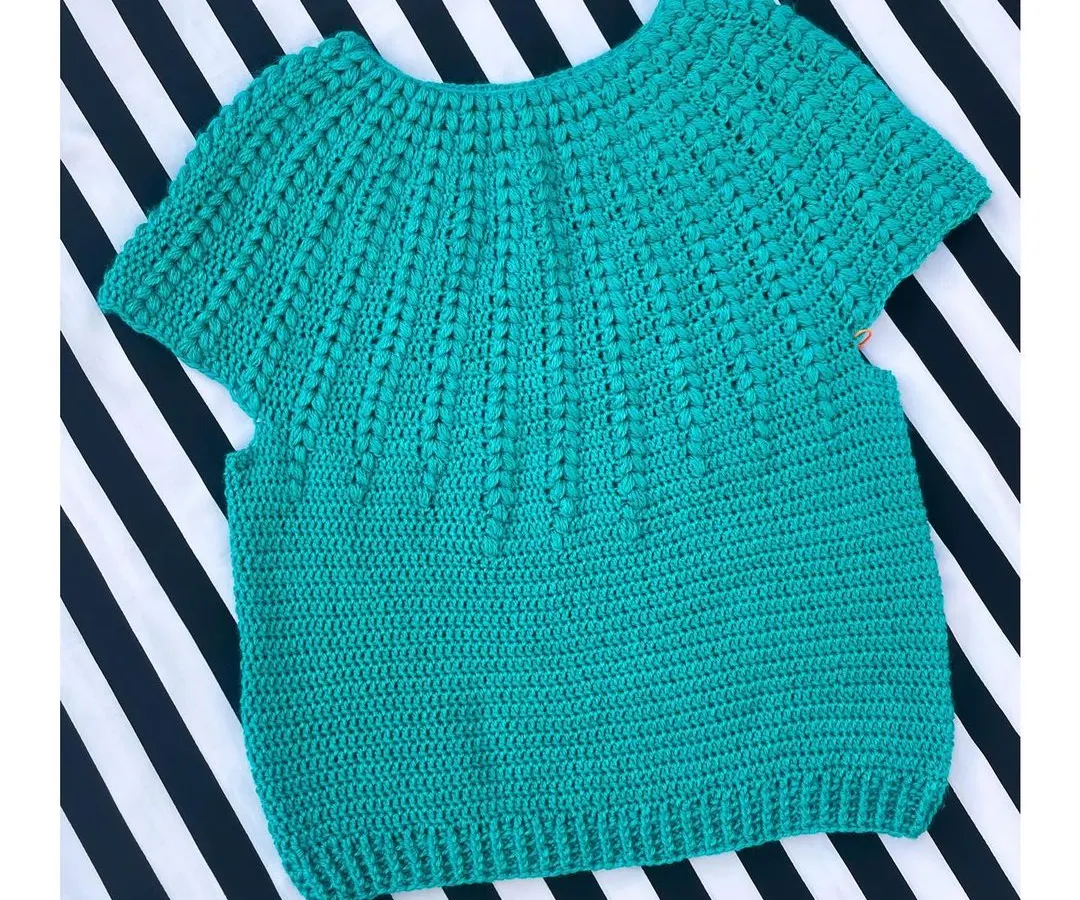 Here is the Goldenrod Sweater, a beautiful short-sleeved top made with soft cotton yarn. The textured stitch work gives it a lovely feel, and it's perfect for a casual day out. This piece is laid flat to show the full body construction before it's worn.