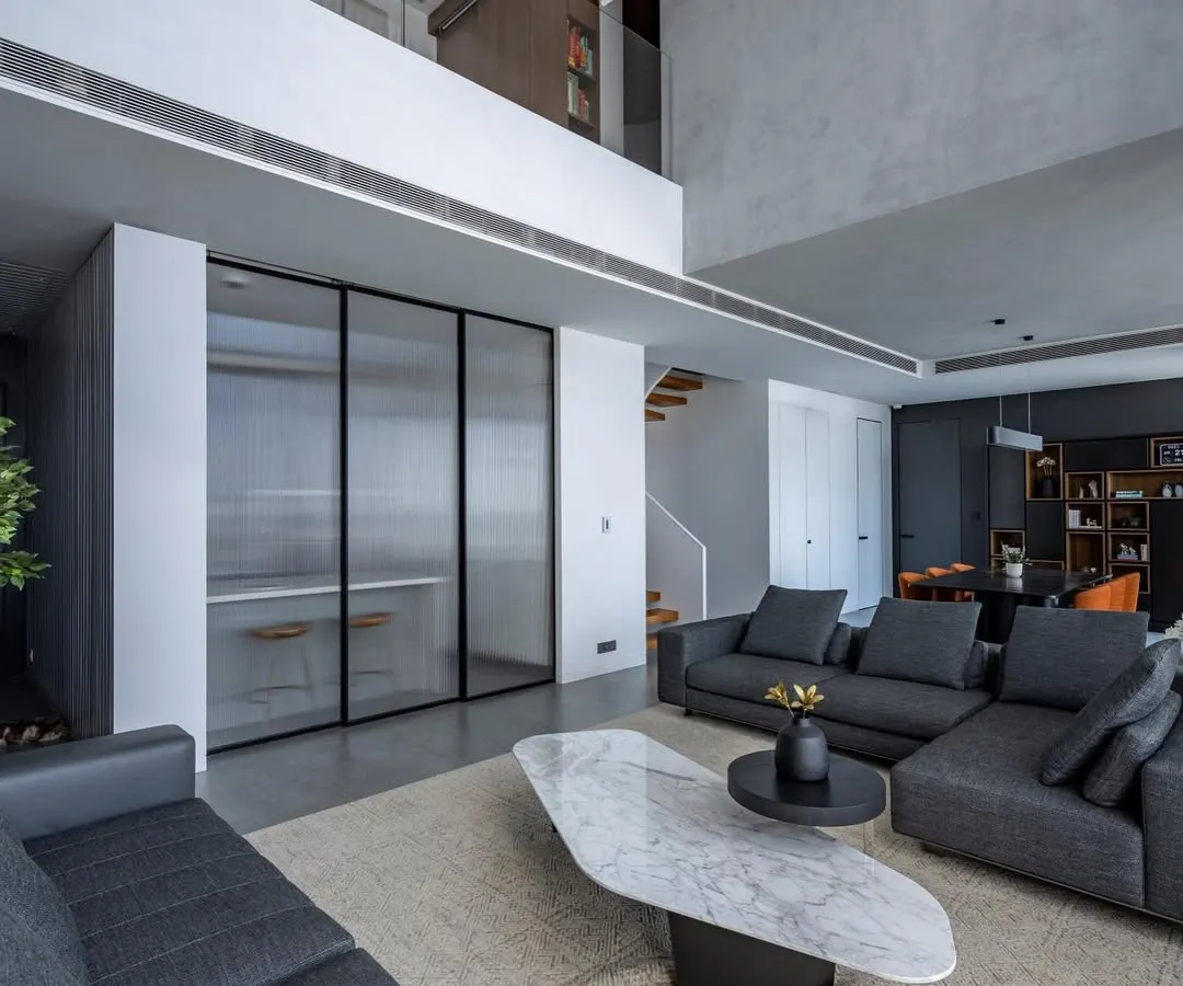 The living area of 'The Grey House', a duplex apartment in Mumbai. We embraced a minimalist aesthetic with a monochromatic grey palette, using textured walls and clean-lined furniture to create a space that is both sophisticated and calming. The double-height ceiling enhances the sense of openness and light.
