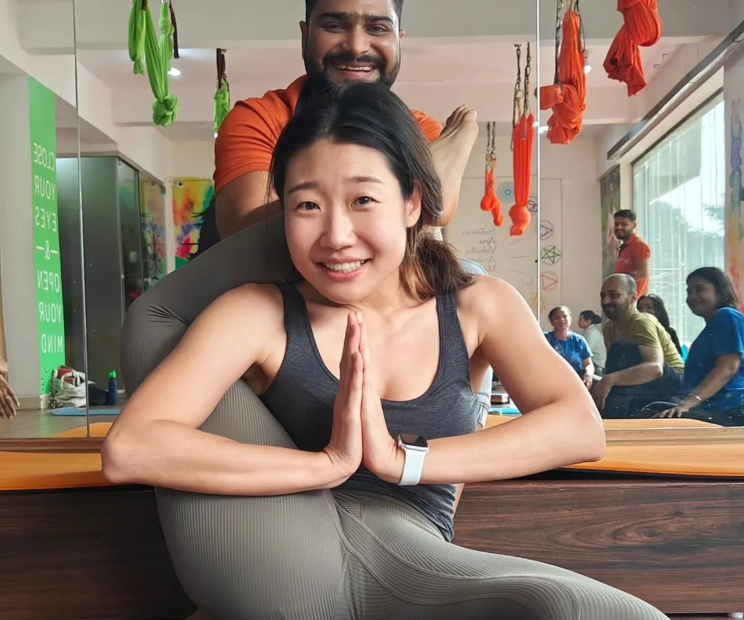 This is a "Jai Ho!" moment. With careful guidance and support, this student achieves the advanced Eka Pada Sirsasana (One-Leg-Behind-Head Pose). Her smile says everything about the joy and confidence that comes from progressing in your practice.